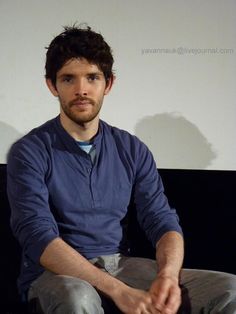 a man sitting on a black couch in front of a projector screen with his hands folded