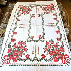 an embroidered tablecloth with bells and poinsettis is on a dining room table