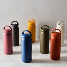 six different colored stainless steel water bottles lined up in a row on a white surface