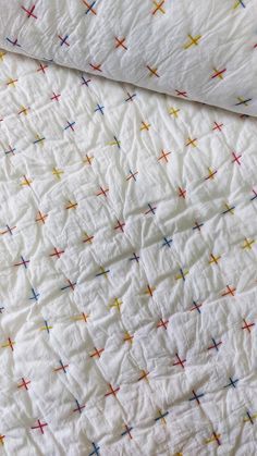 an unmade bed with white sheets and multicolored crosses on it's coverlet