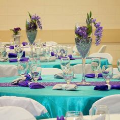 the table is set with purple and white flowers in vases, silverware, and napkins