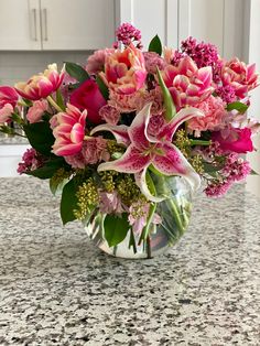 a vase filled with lots of pink flowers on top of a marble countertop in a kitchen