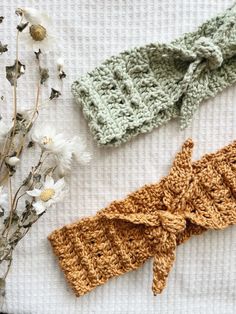 three crocheted headbands laying on top of a table next to flowers