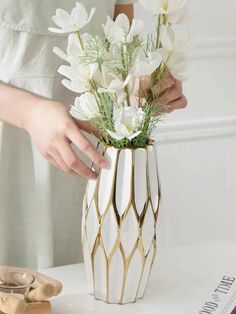 a woman is arranging flowers in a vase on a white table with other items nearby