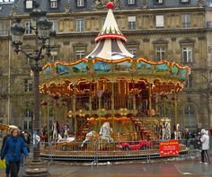 a merry go round in front of a building with people walking around and onlookers