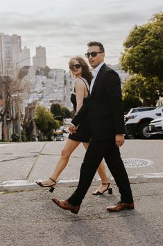 a man and woman are walking down the street in their business attire, one is wearing sunglasses