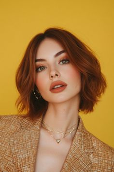 Woman with short red hair and a neutral expression, wearing gold jewelry and a textured jacket, against a yellow background. Tan Skin Auburn Hair, Red Hair Color Short Haircuts, Dark Auburn Hair Short, Hair Color To Make Green Eyes Pop, Short Red Hairstyle Women, Celebrity Red Hair, Auburn Hair Medium Length, Short Red Hair Green Eyes, Auburn Hair Color Short