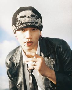 a young man wearing a black leather jacket and hat with his finger in his mouth