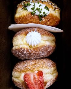 three pastries are stacked on top of each other in a box with powdered sugar and strawberries