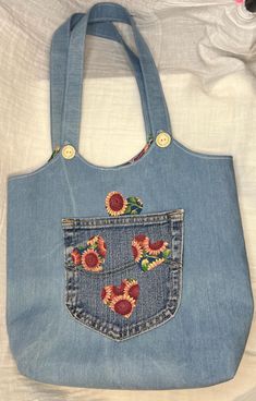 a denim bag with embroidered flowers on the front and back pocket, sitting on a bed