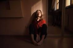 a woman sitting on the floor in front of a door with her eyes closed and looking up