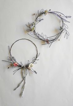 two metal wire wreaths with flowers and leaves on them sitting on a white surface