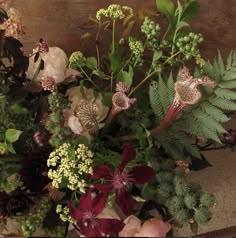 a vase filled with lots of flowers and greenery next to a wooden table top