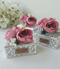 three small silver boxes with pink flowers in them on a table next to white flowers