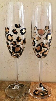 two wine glasses sitting on top of a wooden table next to each other, one with an animal print design