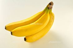 three bananas on a white surface with one banana still attached to the top of it