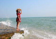 a woman in a straw hat standing on the edge of a pier near the ocean