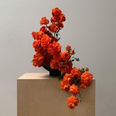 an arrangement of orange flowers sitting on top of a wooden block