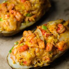 two stuffed eggplant halves with shrimp and vegetables on them are sitting side by side