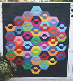 a colorful quilt hanging on the side of a fence next to a potted plant