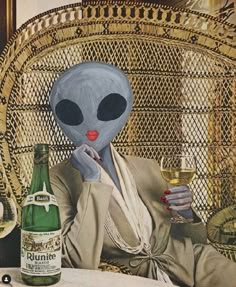 an alien sitting in a chair with a bottle of wine and a glass next to it