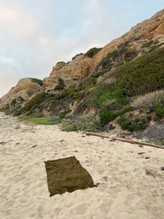 a blanket laying on top of a sandy beach next to a hill covered in vegetation