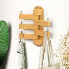 a wooden coat rack hanging on the wall next to a bag and umbrellas in front of a plant