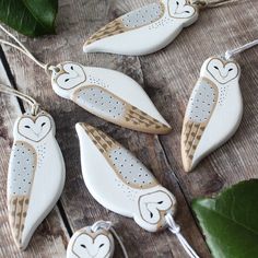 four ceramic owl ornaments hanging from strings on a wooden table next to green leafy leaves