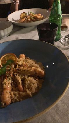 a blue plate topped with rice covered in shrimp and garnished with lemon wedges