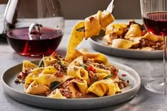 a plate of pasta with meat and vegetables next to a glass of wine on a table