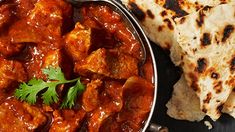 some food is sitting on a table next to bread and pita bread, with a fork in it