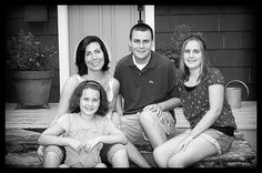 the family is sitting on the steps outside their house smiling at the camera while posing for a black and white photo