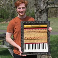 a man holding up an old piano in front of a tree