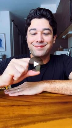 a man sitting at a wooden table with his fingers pointing to the camera and smiling