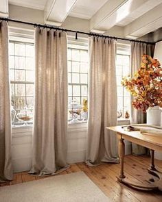 a living room filled with lots of windows covered in curtains and drapes next to a wooden table