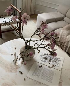 a white table topped with a vase filled with pink flowers next to an open book