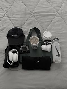 the contents of a duffel bag laid out on a bed with headphones, water bottle and other items