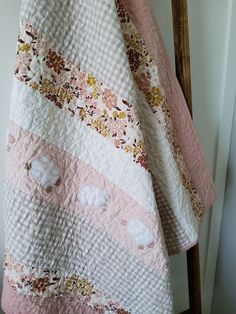 a pink and white quilt hanging on a clothes rack next to a door with a wooden frame