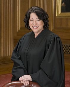 a woman in a black robe is sitting on a brown chair and smiling at the camera