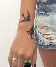 a woman's hand with a bird tattoo on the left wrist and an arrow in the middle