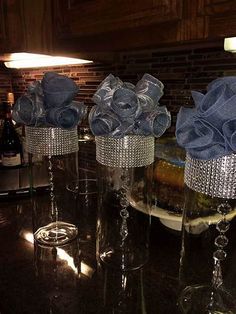 three crystal vases with blue flowers in them sitting on a counter next to a wine bottle