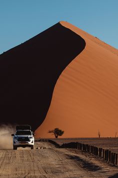 a white car driving down a dirt road next to a tall sand dune in the desert