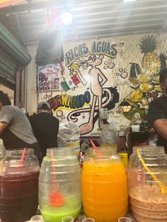 people are standing at a juice stand with many different types of drinks in plastic containers