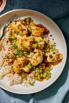 a white plate topped with rice covered in shrimp and peas next to a bowl of sauce