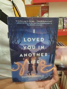 a person holding up a book in front of bookshelves with the title i loved you in another life