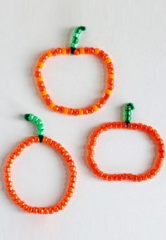 three orange and green beaded bracelets on a white surface with two small beads attached to them