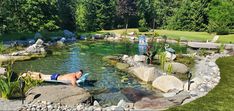 a man laying on top of a large rock next to a small pond filled with water