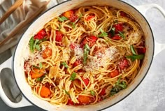 a large pot filled with pasta and vegetables on top of a table next to bread