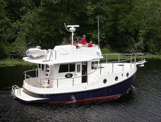 a white and blue boat floating on top of a river next to lush green trees