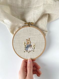 a hand holding up a small embroidery hoop with an image of a mouse on it